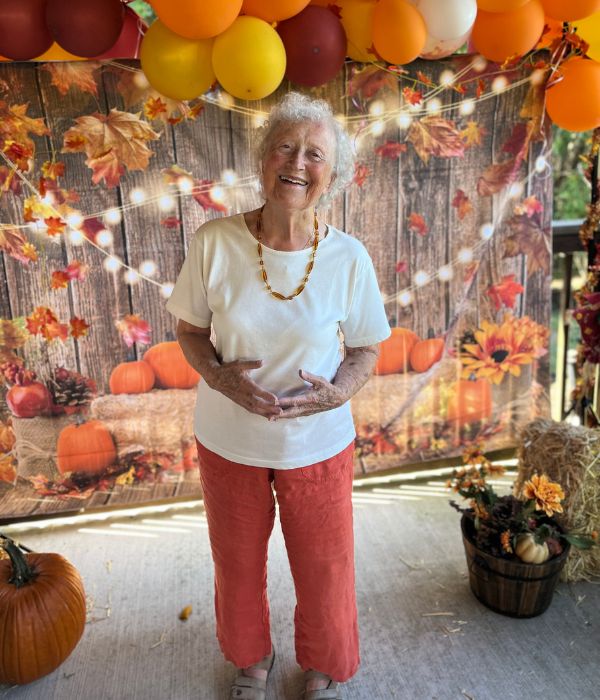 older woman standing and smiling in front of a fall setting and balloons