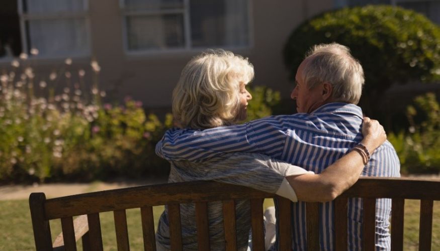 older couple sitting together on a bench with their backs to us