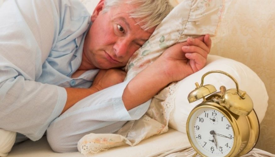 older man in bed having a hard time falling asleep staring at an alarm clock
