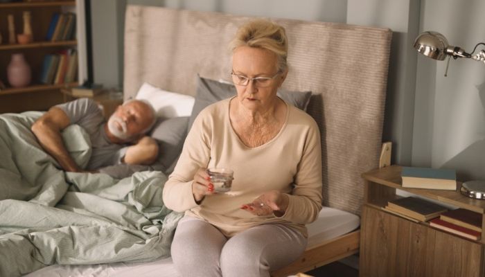woman sitting on her bed looking at her pills 