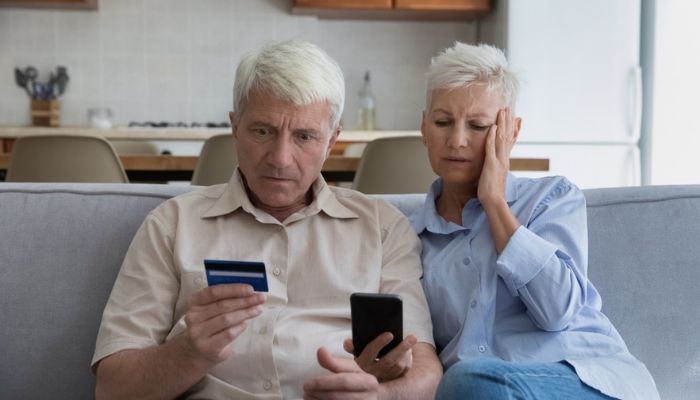 elderly couple sitting with a credit card and laptop realizing they were scammed